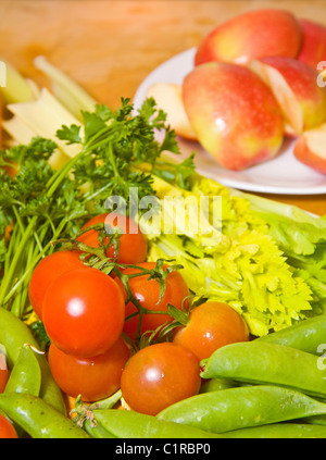 Colorful fresh vegetables and sliced apples on a wooden cutting block in the kitchen Stock Photo