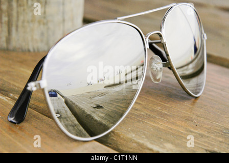 Sunglasses on wooden beach with beach in reflected in lens.