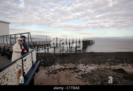 A couple of tourists enjoy the view from Mumbles Pier under a dramatic cloudy sky, near Swansea, south Wales Stock Photo