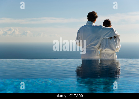 Couple standing at edge of infinity pool, looking at view Stock Photo