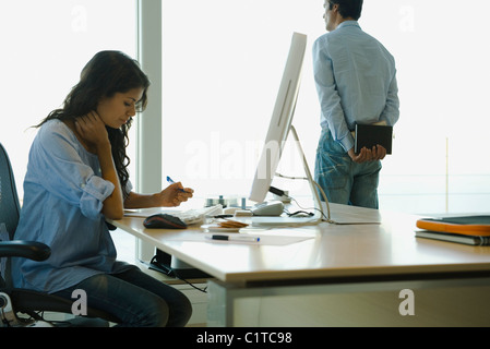 Woman working at desk at home, husband looking out window in background Stock Photo