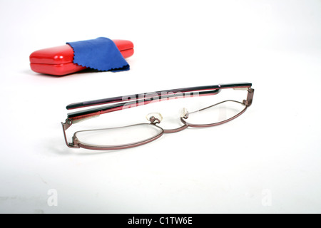A pair of burgundy reading glasses on a white cut out background with a red glasses case and blue cleaning cloth. Stock Photo