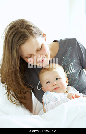 Portrait of a happy mother hugging her baby while relaxing in bed