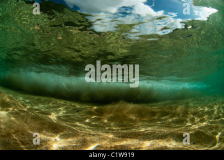 Underwater wide shot of a wave breaking on the sandy ocean bottom floor. Stock Photo