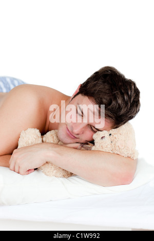 Young man in pajamas sleeping with a teddy bear lying on his bed Stock Photo