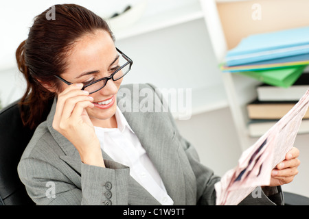 Cheerful businesswoman holding her glasses and reading a newspaper in her office Stock Photo