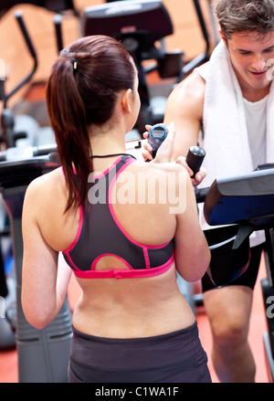 Female trainer holding a chronometer while man exercising on a bicycle Stock Photo