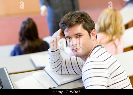 Handsome male student smiling at the camera during an university lesson Stock Photo