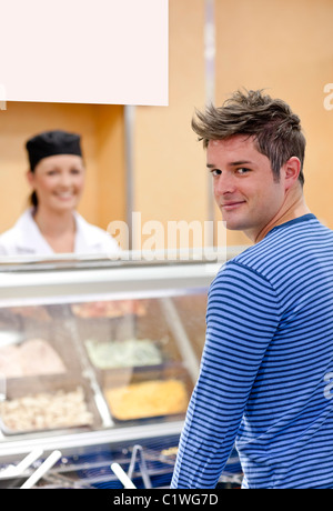 Handsome customer standing in the queue in a cafeteria smiling at the camera Stock Photo