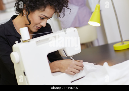 Young hispanic female dressmaker using sewing machine. Horizontal shape, side view, waist up Stock Photo