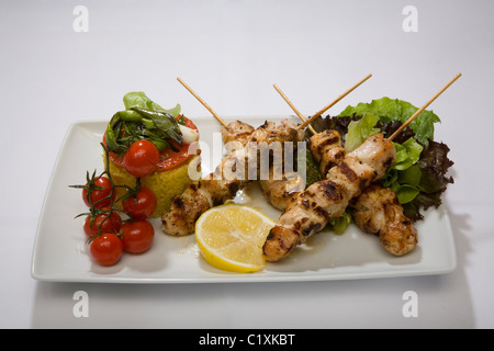 Skewered meat chicken tomatoes lemon lettuce yellow rice plate eat food eating white background onion cuisine appetite meal four Stock Photo