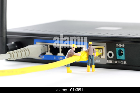 Connected - Macro photo of two tiny toy engineers connecting a wire to a router. Stock Photo