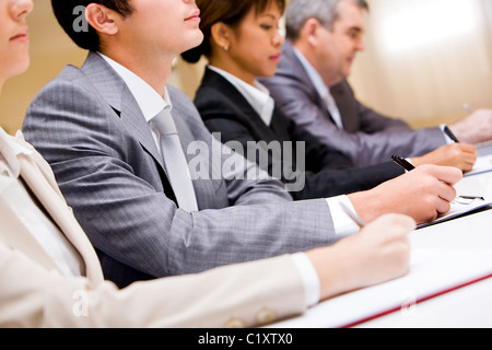 Row of business people making notes during conference Stock Photo