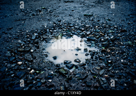 A pothole in the road full of rain water Stock Photo