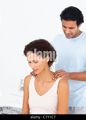 Hispanic man massaging his girlfriend sitting on their bed Stock Photo