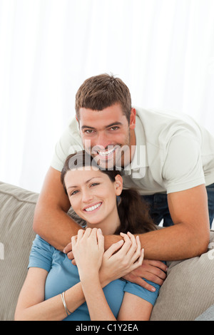 Happy man hugging his girlfriend sitting on the sofa Stock Photo