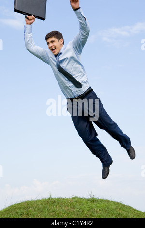 Handsome businessman leaping over green grass with blue sky at background Stock Photo