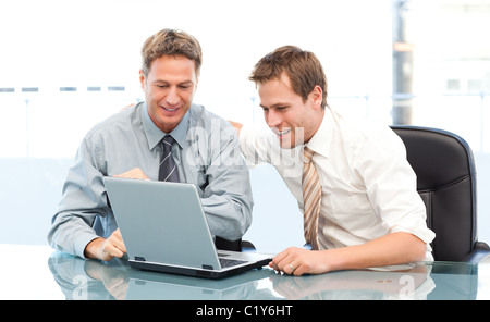 Two happy businessmen working together on a laptop sitting at a table Stock Photo