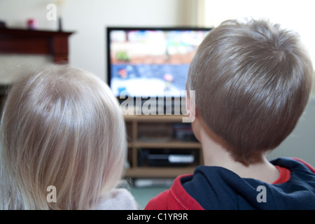 A young brother and sister watch TV together in the family home England UK Stock Photo