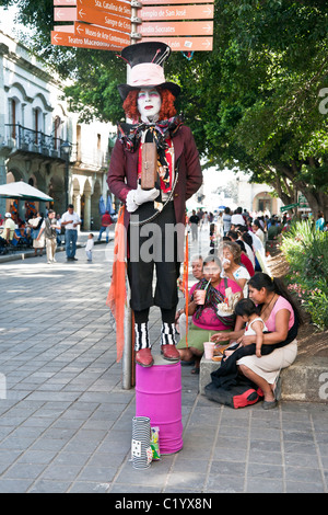 mad hatter mime in extravagant Victorian costume whiteface & red wig stands in Oaxaca Zocalo holding box of destinies Mexico Stock Photo