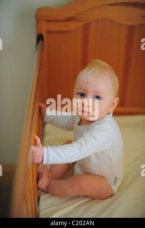 A one year old baby boy sitting in his cot at home in a bedroom or nursery Stock Photo