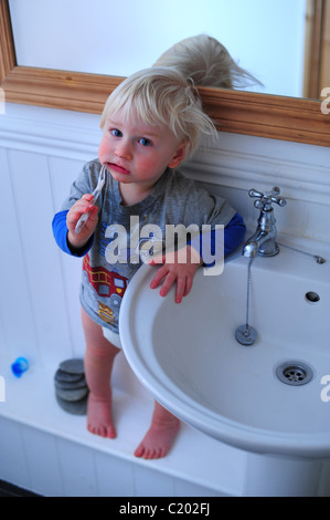 A two year old boy cleaning his teeth with a toothbrush in the bathroom Stock Photo