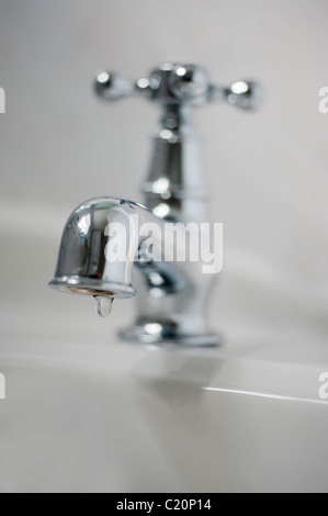 Metal tap in white bathroom with dripping water. Stock Photo