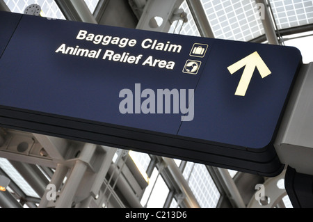 A dark blue sign at an airport that reads baggage claim and animal relief area with symbols and a directional arrow in white Stock Photo