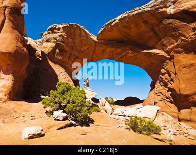 A man and woman stand together on a rock below Broken Arch posing for the camera, Arches National Park, Utah, USA. Stock Photo
