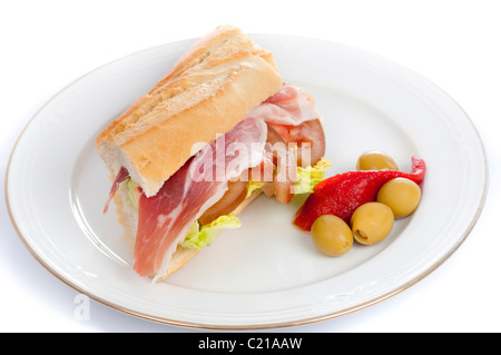 Baguette sandwich with spanish jamon serrano, lettuce, olives and peppers an a white plat. Stock Photo