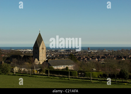 The Anglo-Saxon church of St Mary, Sompting, Sussex, nestling on the Downs with Sompting & Lancing and the sea in the background Stock Photo