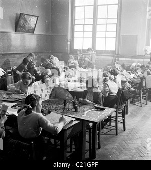 1950s, historical, primary school children sitting at desks in classroom doing activities; drawing, painting and make paper models, England, UK. Stock Photo