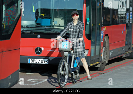 A smart lady waiting to start cycling on a Boris Bike amongst red London buses Stock Photo