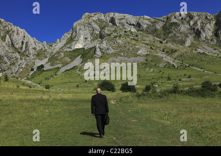 Businessman outdoors walking through a big mountain.The main focus is on the rocks,the man is slightly out of focus. Stock Photo