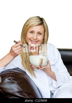 Charming woman eating cereals on the sofa against white background Stock Photo