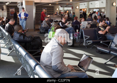 People waiting for their flight at the gate of New Orleans Airport terminal, reading and using technology Stock Photo