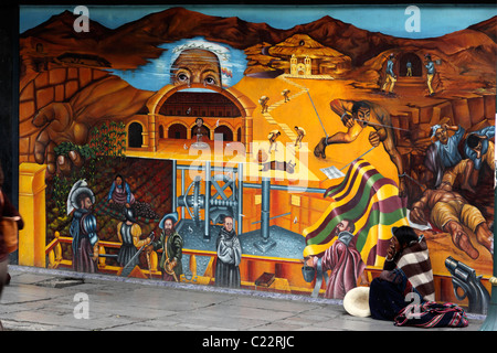 Lady from Potosi region begging in front of mural showing repression of natives in Potosi silver mines back in colonial times, La Paz, Bolivia Stock Photo