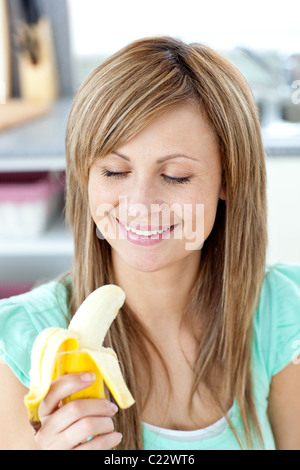Smiling young woman holding a banana in the kitchen Stock Photo