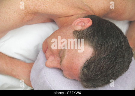 A man laying with his face to the side on a headrest, arms up on a massage table, waiting to be massaged. Mature white male waiting on a massage table Stock Photo