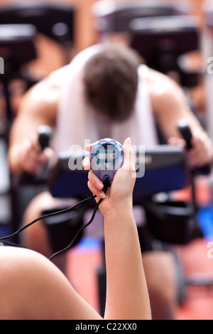 Close-up of a young woman holding a chronometer and man doing physical exercise Stock Photo