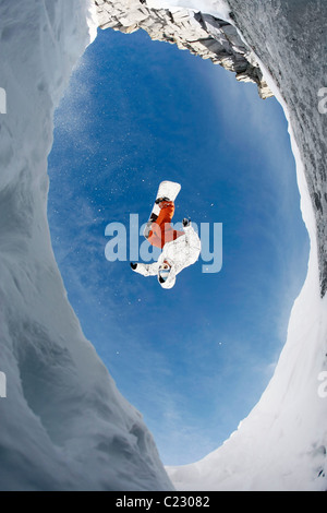 View from below of snowboarder jumping over rocky mountainside in winter Stock Photo