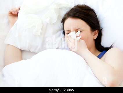 Sick young woman using a tissue lying in a bed