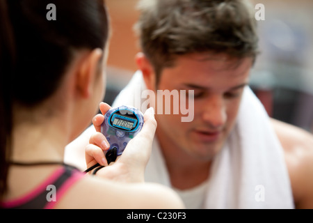 Female trainer holding a chronometer while man doing physical exercise Stock Photo