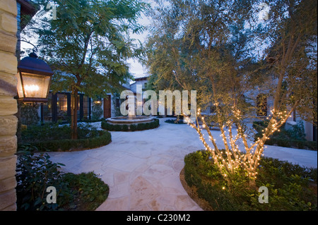 House exterior at night with a fountain:a lantern and trees:one in which is lit with fairy lights Stock Photo