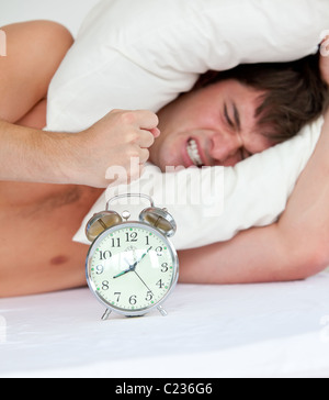 Angry man stressed by his alarm clock lying on his bed Stock Photo
