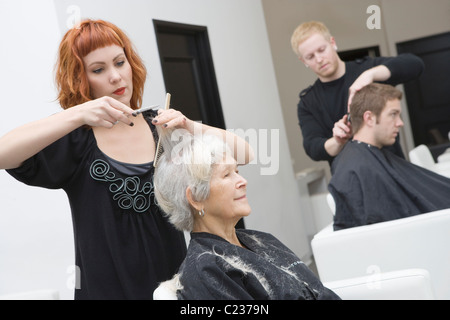Stylist cuts elderly woman's hair Stock Photo
