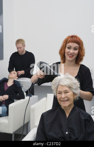 Stylist blow-drys elderly woman's hair Stock Photo