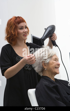 Stylist blow-drys elderly woman's hair Stock Photo