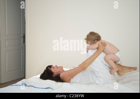 A mother laying down with legs bent holding a toddler on them Stock Photo