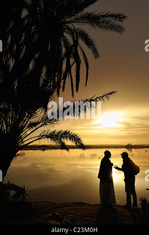 Two Egyptians talking during a sunset over a salt lake in Fatnas Island near the town of Siwa, western desert, Egypt Stock Photo